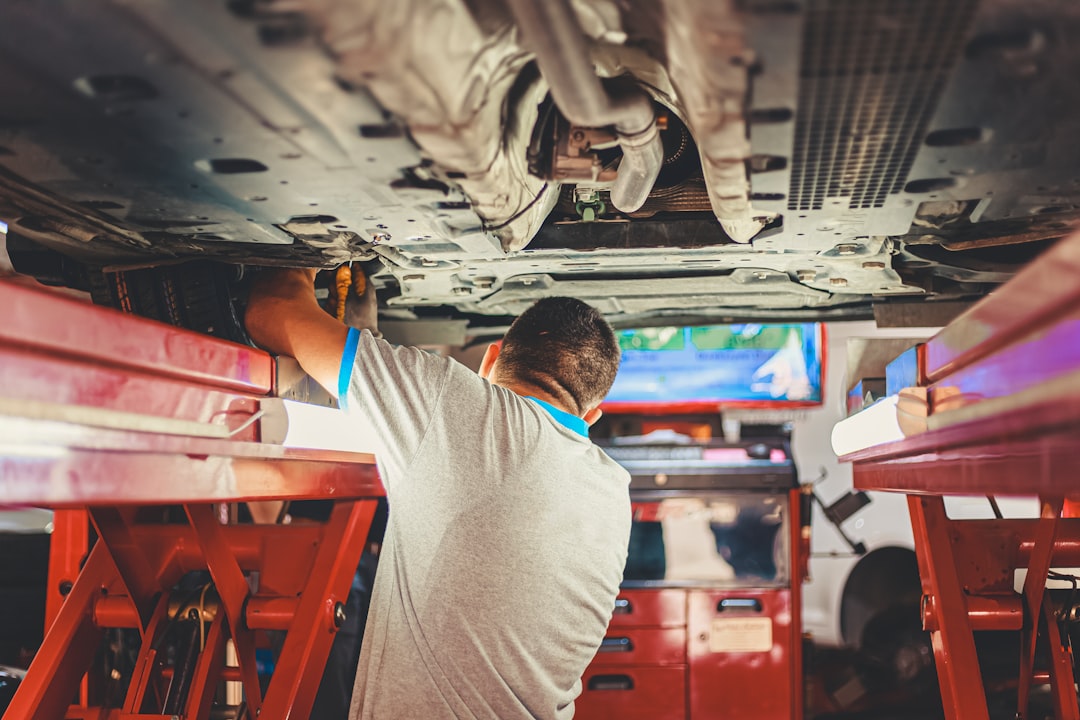 Technician working beneath a vehicle on a lift inside an auto repair shop